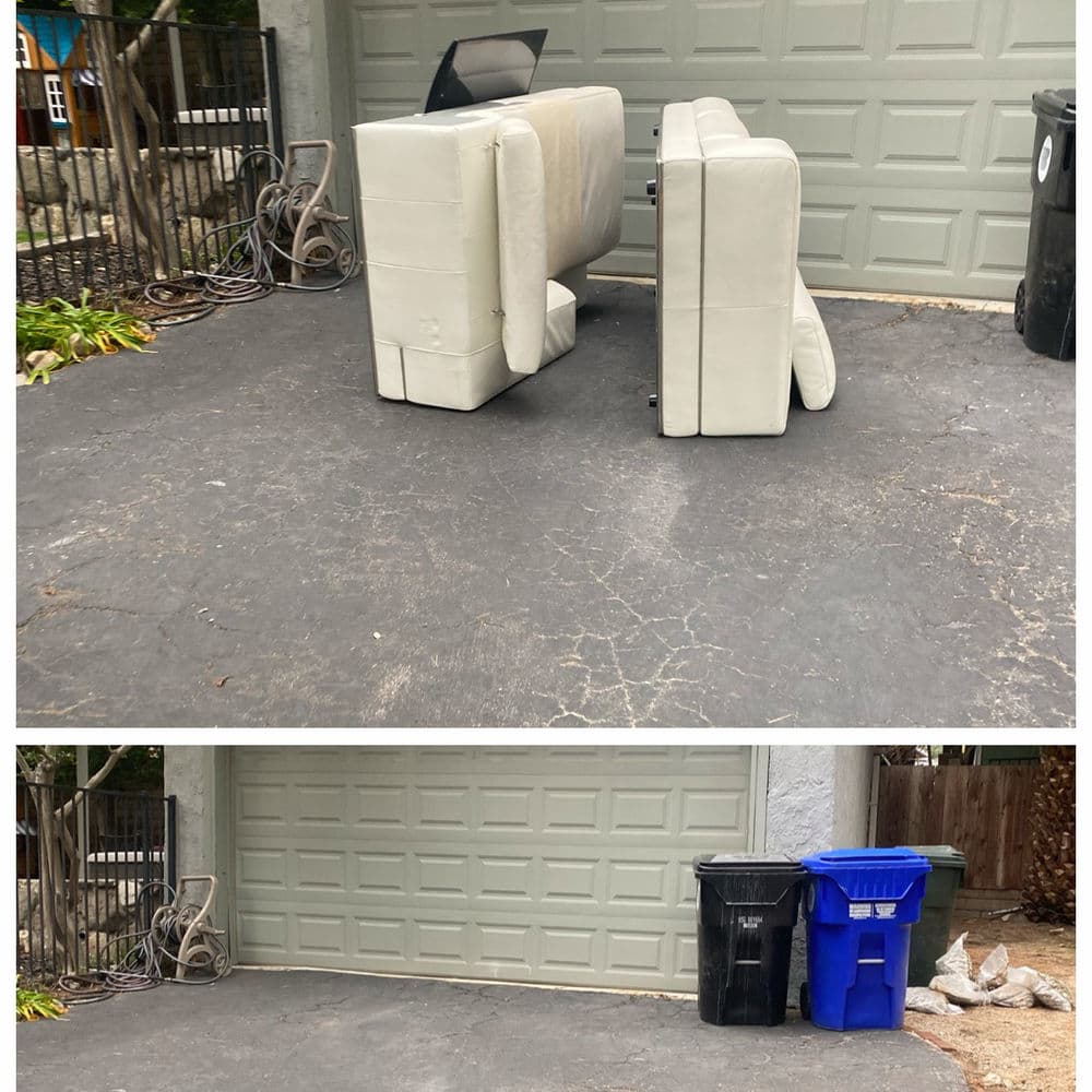 Abandoned white sofa and two trash bins in a driveway next to a garage door.